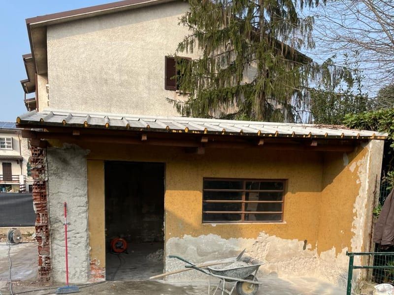 Prima: il deposito attrezzi con l’intonaco giallo scrostato, i mattoni a vista sul lato, la vecchia copertura e il vano della porta senza serramento